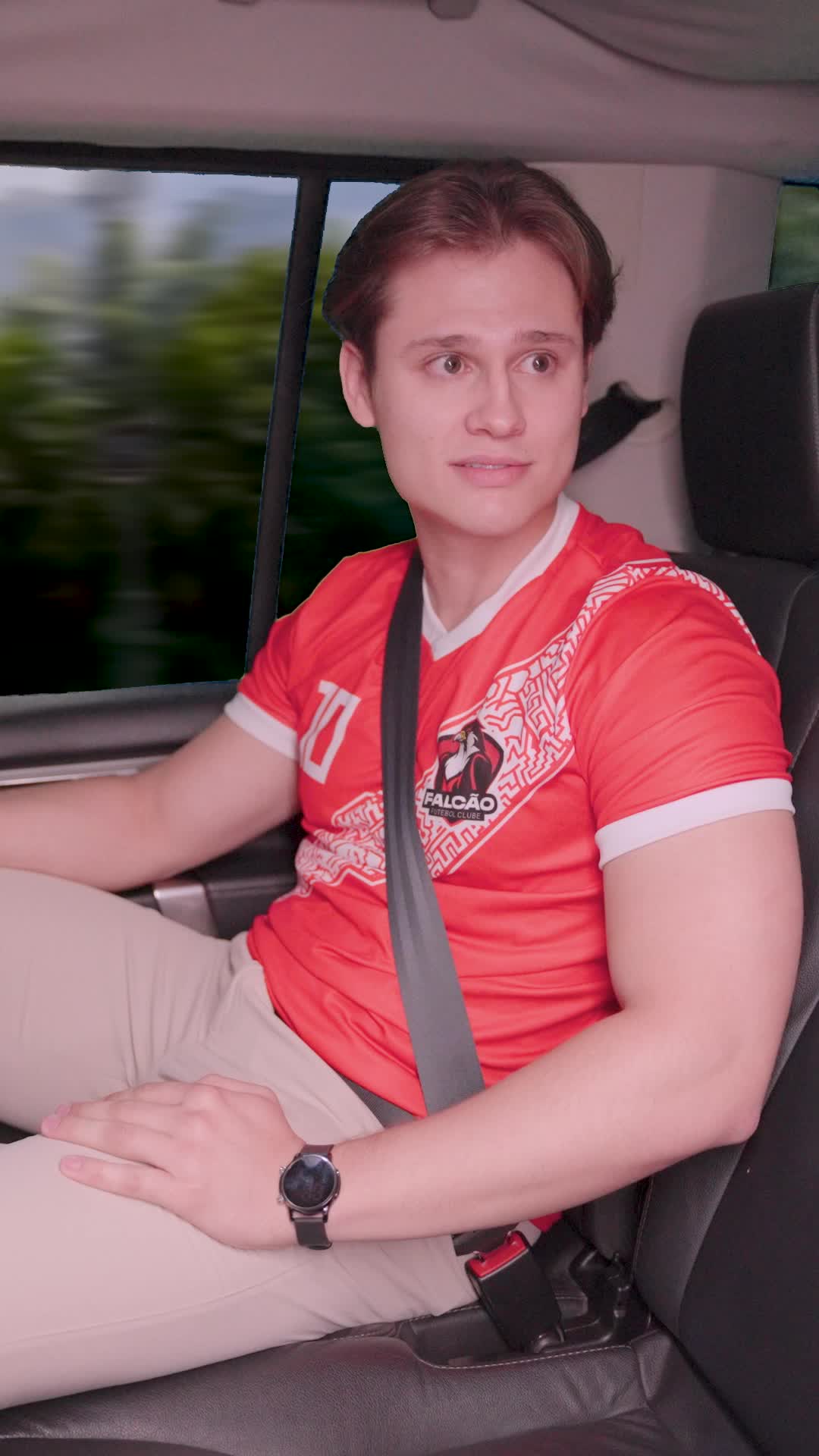 Jogador jovem e loiro com a camisa vermelha número 10 do Falcão Futebol Clube, sentado no banco de trás de um carro