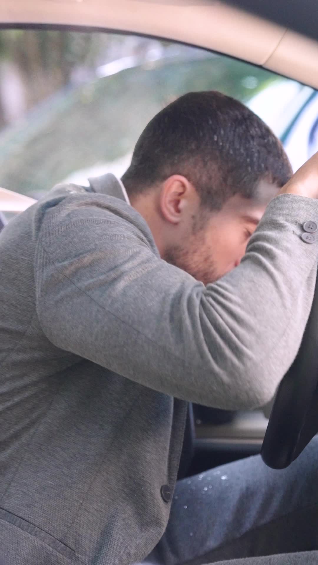 Lucas Moreti, de cardigã cinza, com a cabeça apoiada no volante dentro do carro